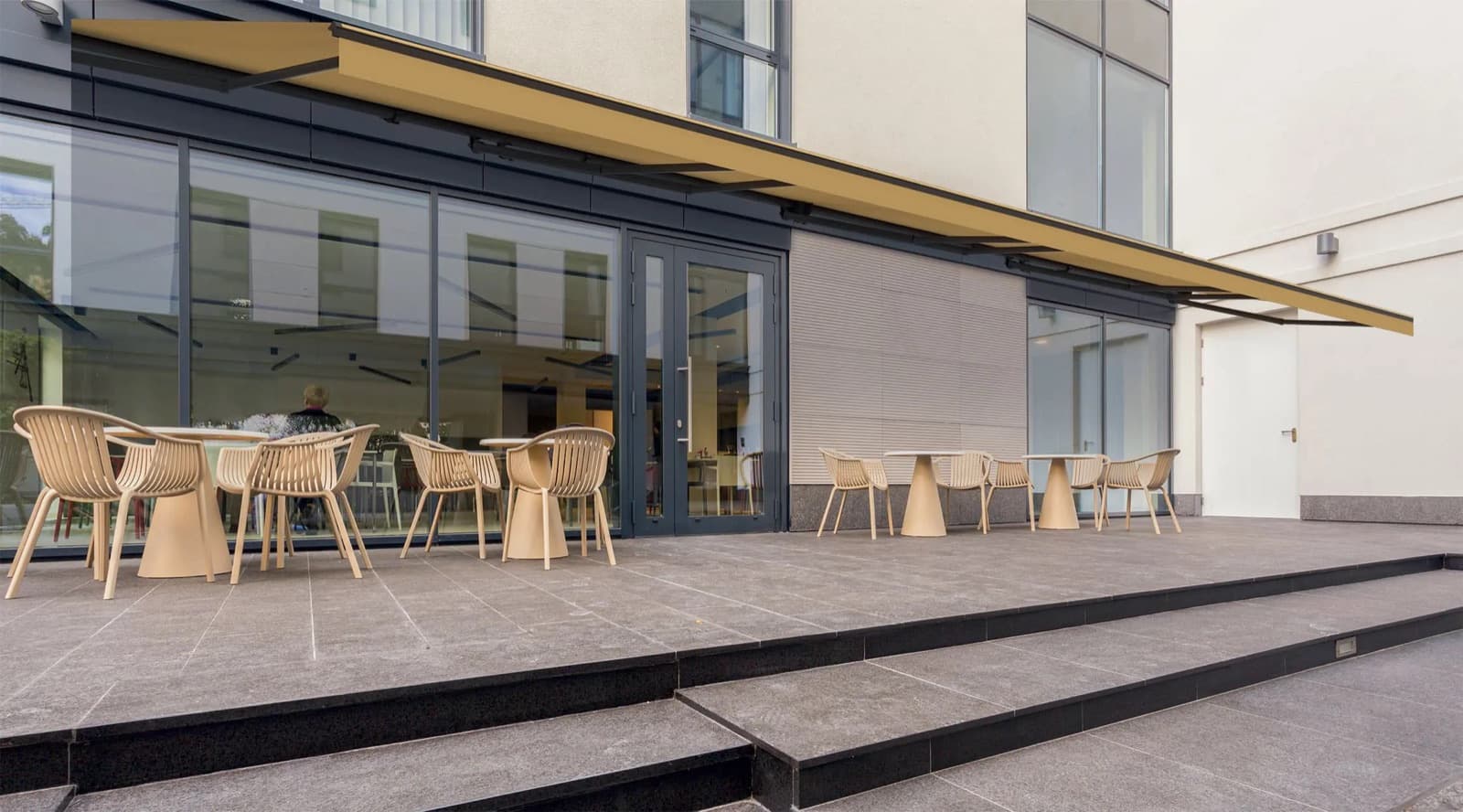 Grande terrasse de café ombragée par un store banne, tables dressées en dessous